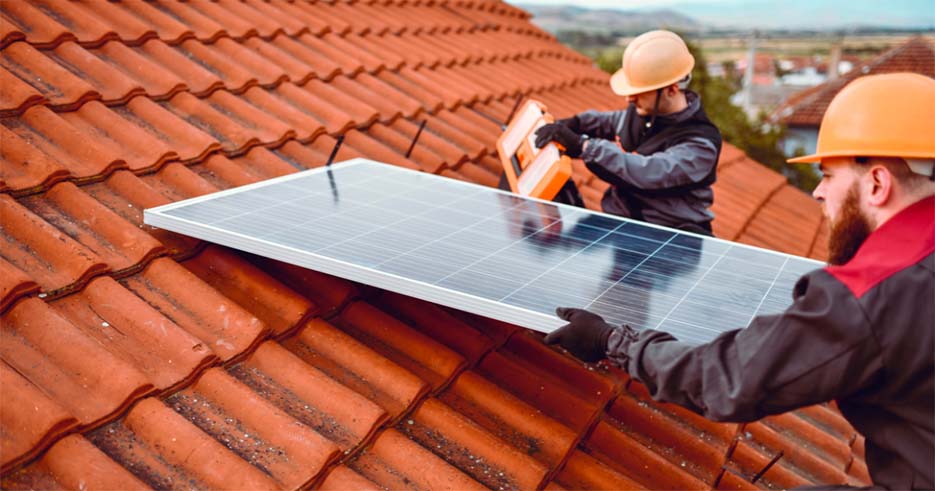 Two technicians in safety gear installing solar panels on a rooftop